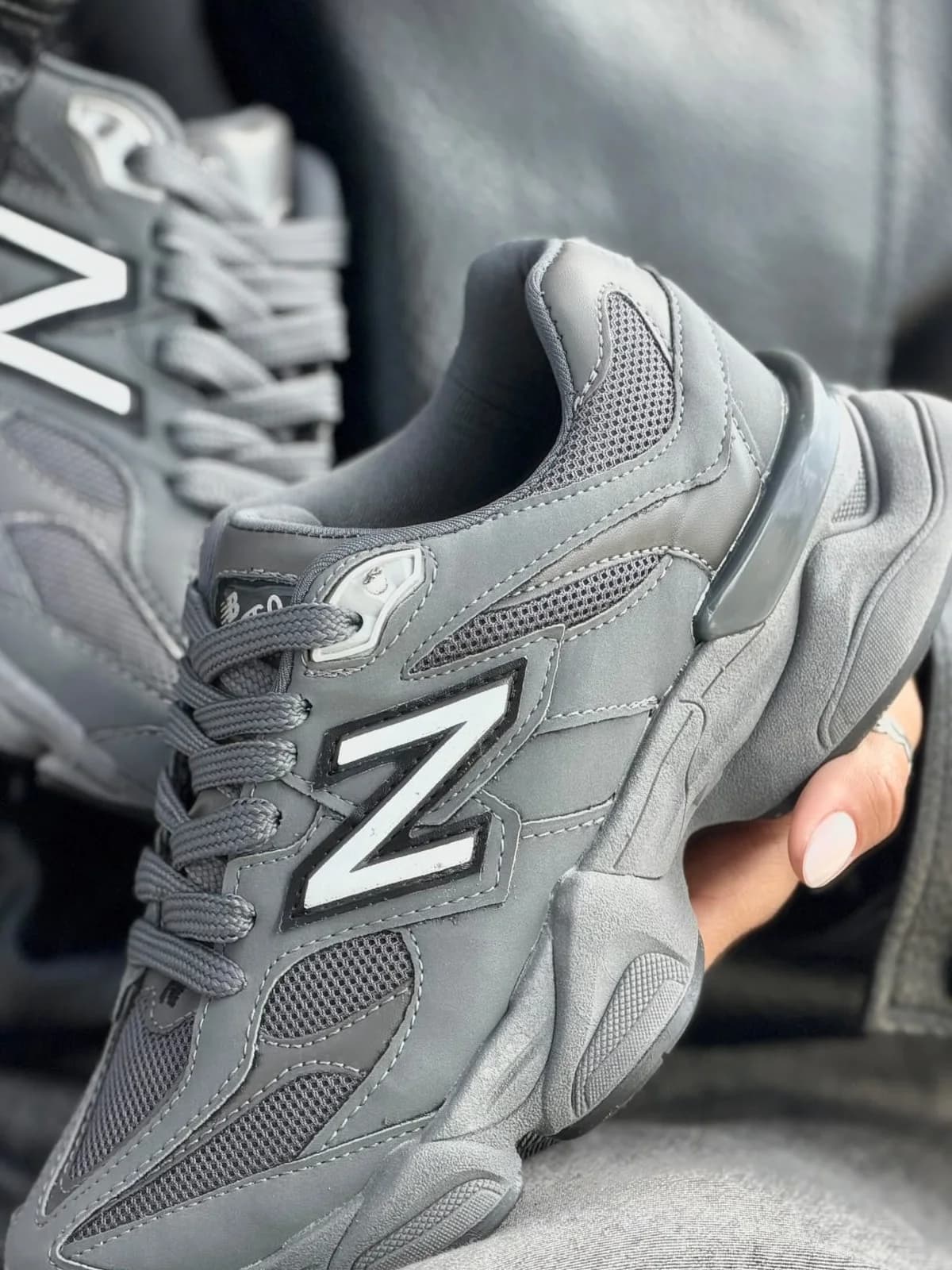Uma mão segurando um New Balance 9060 cinza